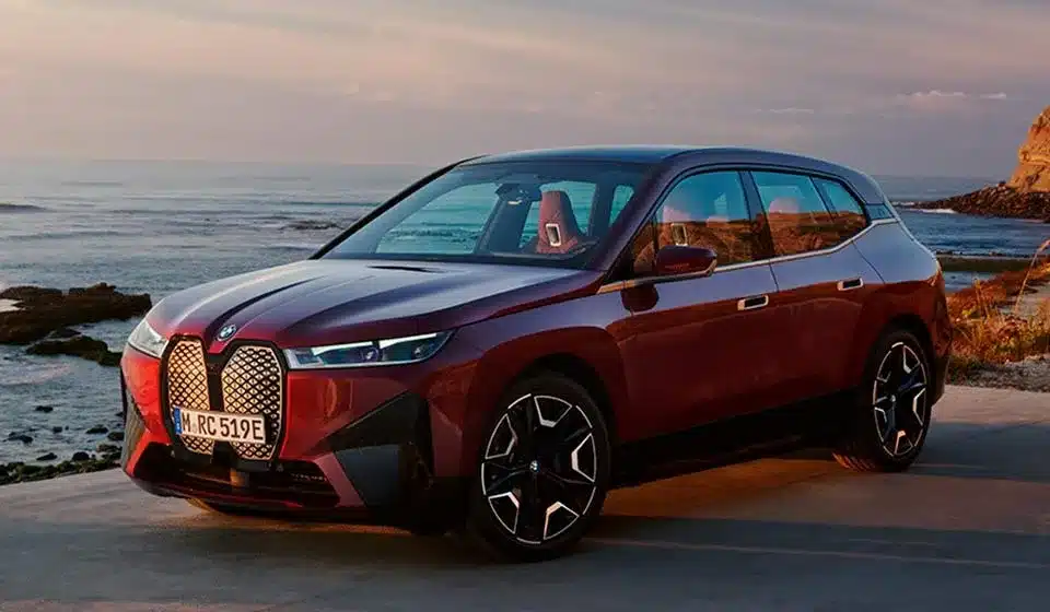 BMW iX vermelho estacionado à beira-mar ao pôr do sol, SUV elétrico premium com mais de 700 km de autonomia.
