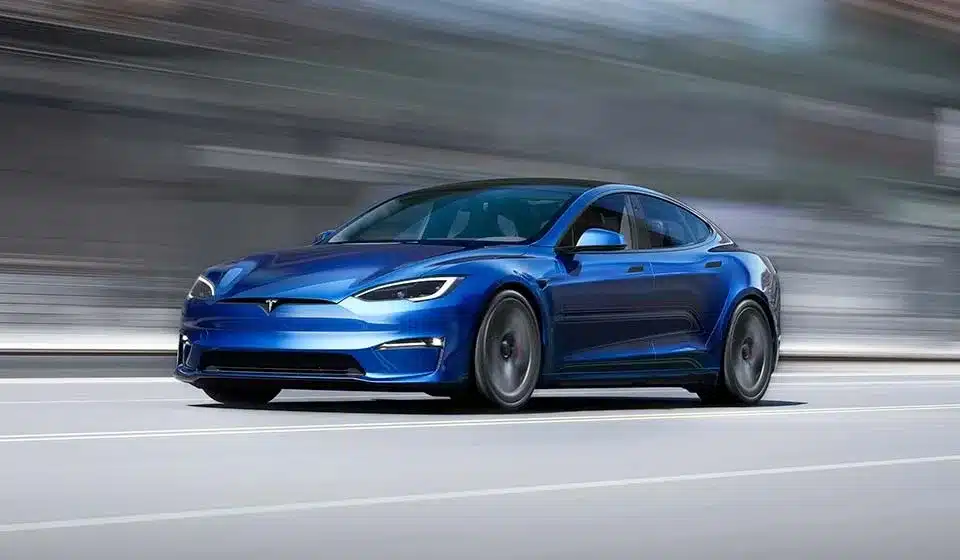 Tesla Model S azul em movimento numa estrada urbana, berlina elétrica de alta performance com até 652 km de autonomia WLTP.